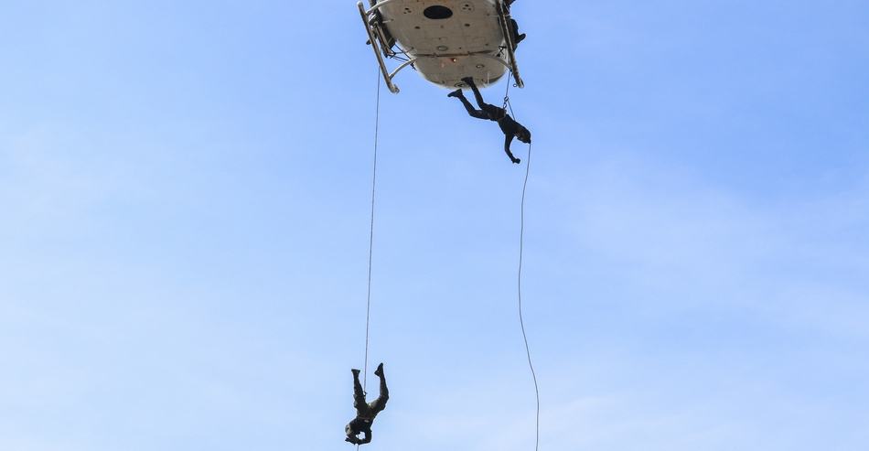 Two soldiers rappelling from a helicopter face-first in a military rappel