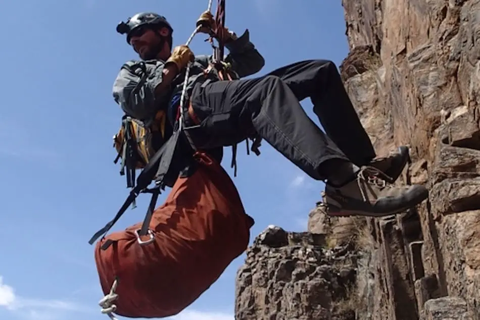 A man rappelling with a haul bag attached to his harness